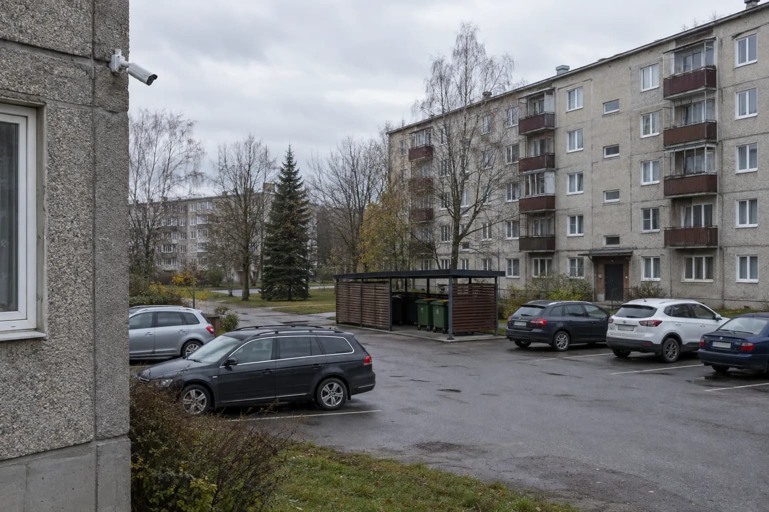 Nõukogudeaegse kortermaja taga parkla ja prügimaja, hoone nurgal valvekaamera
